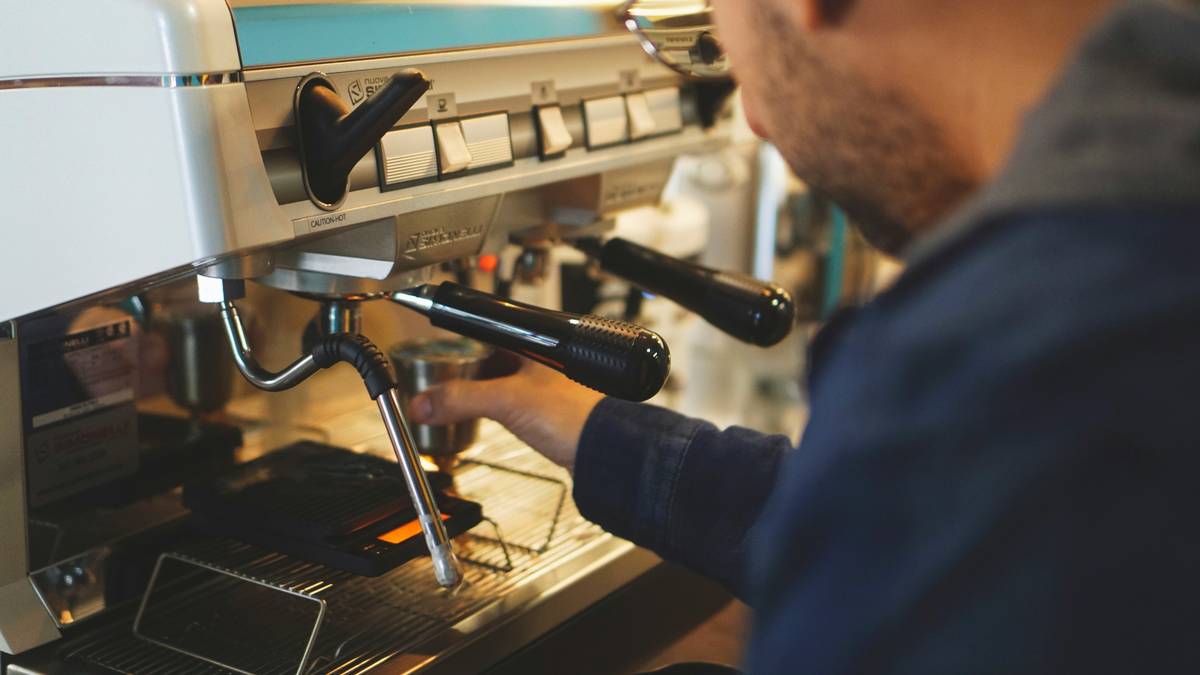 A hand holding freshly ground coffee next to a sleek smart coffee maker.