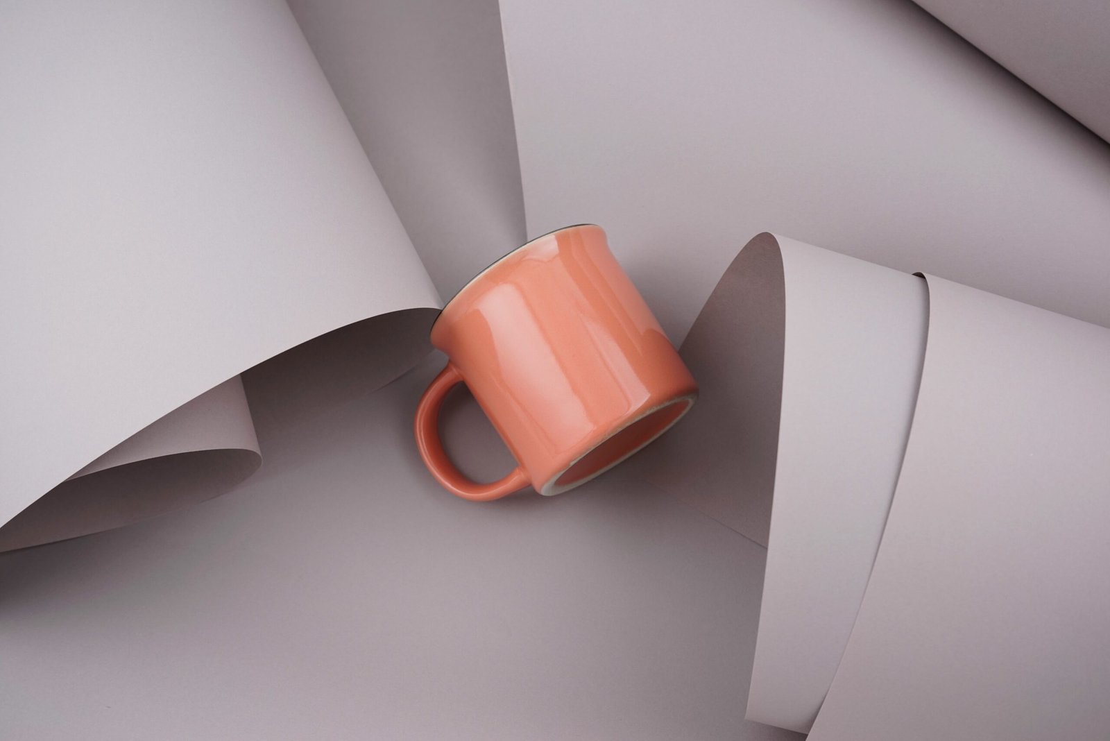 Pastel orange cup, mug flat lay on gray beige papers texture abstract background. Creativity, minimal style concept.